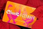 Cluck N Cleaver gift card featuring vibrant orange and pink colors with chicken graphics, surrounded by red fabric, highlighting the perfect gift for delicious scratch-made meals.
